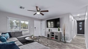 A modern living room with a sofa, coffee table, TV, and a ceiling fan. - Family Fun Getaway Near ASU & Phoenix Zoo (Tempe)