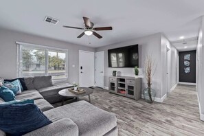 A modern living room with a sofa, coffee table, TV, and a ceiling fan. - Family Fun Getaway Near ASU & Phoenix Zoo (Tempe)