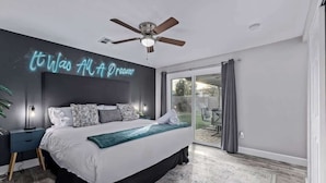 A bedroom with a bed, a ceiling fan, a neon sign, a nightstand, and a view of the outdoors. - Family Fun Getaway Near ASU & Phoenix Zoo (Tempe)