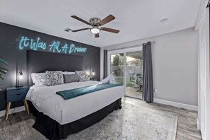 A bedroom with a bed, a ceiling fan, a neon sign, a nightstand, and a view of the outdoors. - Family Fun Getaway Near ASU & Phoenix Zoo (Tempe)