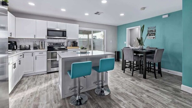 A modern kitchen with white cabinets, a central island with bar stools, and a dining area with a table and chairs. - Family Fun Getaway Near ASU & Phoenix Zoo (Tempe)