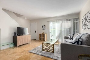 Ein modernes Wohnzimmer mit einer Couch, einem Glastisch, einem Fernseher auf einer Holzkommode und einer Treppe.
