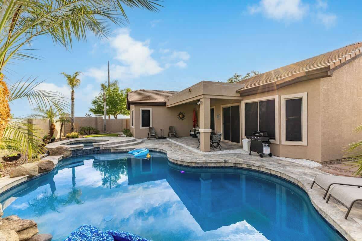 A swimming pool with a patio area, a covered outdoor seating area, and a building with large windows.