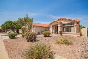 A two-story house with a tiled roof, a driveway, and a landscaped garden with various plants. - Chandler 4BR Getaway w/ Pool, Games & Fast Wi-Fi (Chandler)