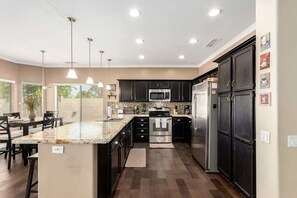 A modern kitchen with dark cabinets, stainless steel appliances, and pendant lighting. - Chandler 4BR Getaway w/ Pool, Games & Fast Wi-Fi (Chandler)
