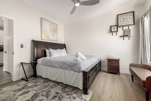 A bedroom with a bed, bedside tables, a chair, a ceiling fan, and artwork on the walls. - Modern 2BR Townhouse |Shared Pool, Gym, Spa & More (Phoenix)