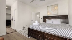 Een slaapkamer met een bed, een plafondventilator, een kunstwerk aan de muur en een deur naar een andere kamer.