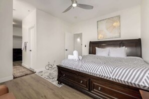 Ein Schlafzimmer mit einem Bett, einem Deckenventilator, einem Wandbild und einer Tür zu einem anderen Raum.