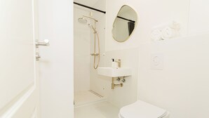 Un baño con inodoro, lavabo, ducha y espejo.