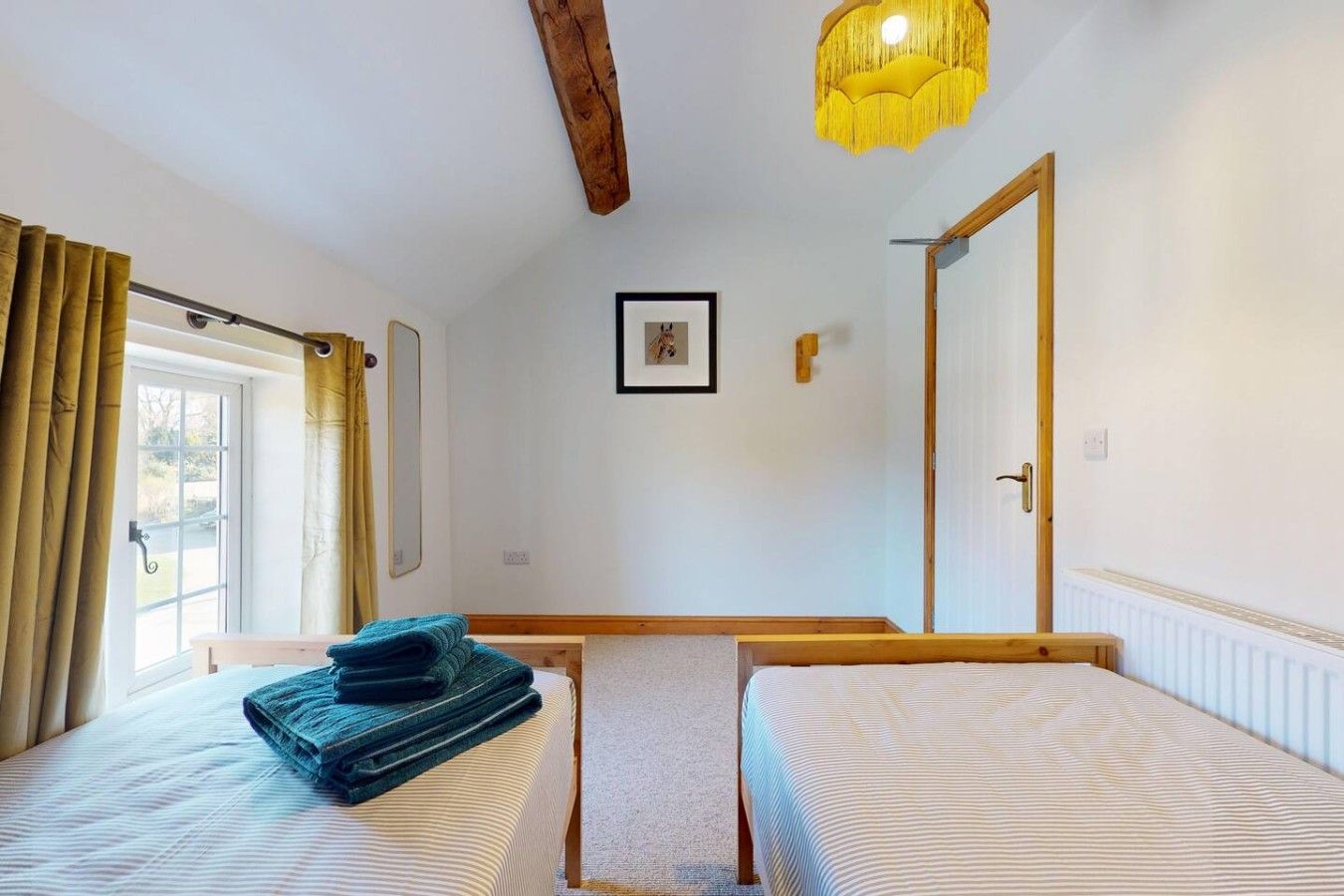 A room with two beds, a wooden ceiling beam, a hanging light fixture, and a door.
