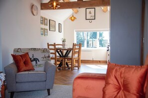 A cozy living room with a sofa, a dining table with chairs, a wooden ceiling, and a window with a view. - The Winners Enclosure: Countryside Flat Above a Village Pub (Withington)