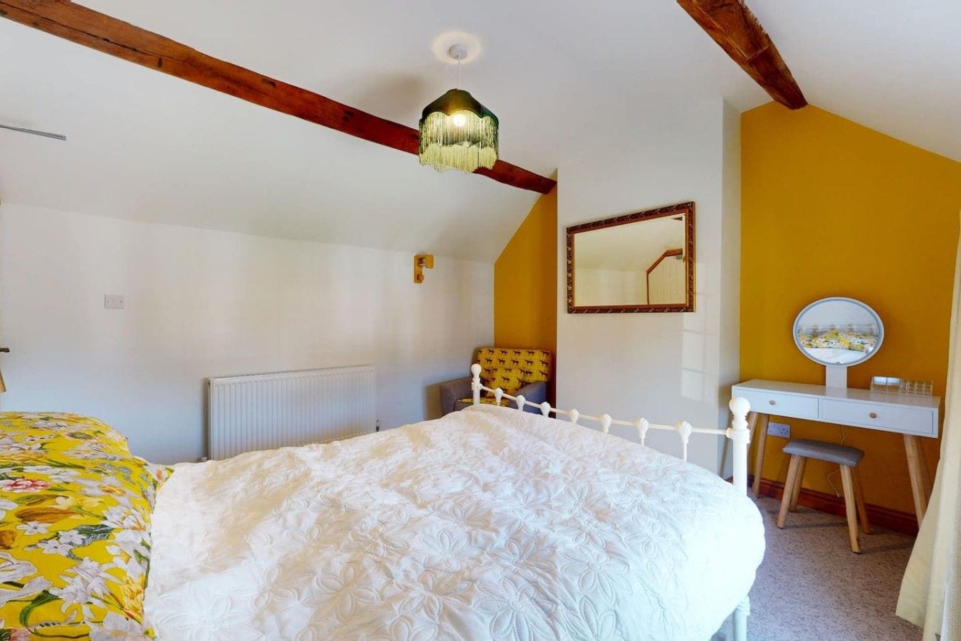A bedroom with a bed, a desk, a chair, a mirror, and a hanging light fixture.