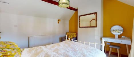 A bedroom with a bed, a desk, a chair, a mirror, and a hanging light fixture.