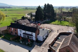 Il s’agit d’une propriété rurale qui comprend un pub appelé « Hare & Hounds », une cour clôturée et un grand champ ouvert en arrière-plan.