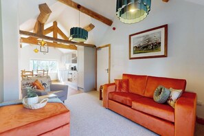 A living room with a red sofa, a wooden ceiling, and a framed picture on the wall. - The Winners Enclosure: Countryside Flat Above a Village Pub (Withington)
