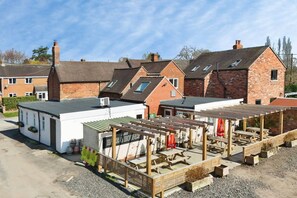 A courtyard with a covered seating area, a small building labeled 'HAVE & HOUNICS,' and brick houses in the background. - The Winners Enclosure · Dog-Friendly Pub Flat (Withington)