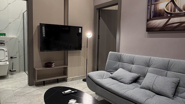 Ett modernt vardagsrum med en grå soffa, ett svart soffbord, en platt-TV och en tavla på väggen.