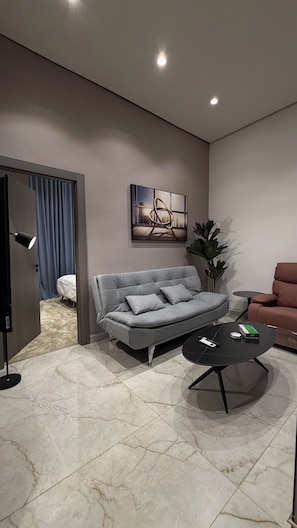 Een moderne woonkamer met een grijze bank, een zwarte salontafel en een schilderij aan de muur.