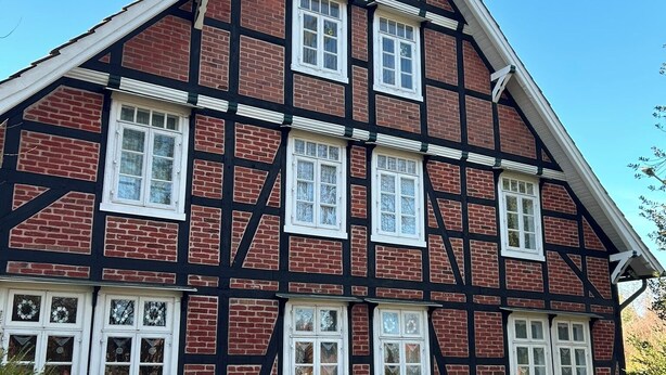 A traditional half-timbered building with multiple windows and a white picket fence. - Central and quiet: freshly renovated old apartment with charm (Helpsen)