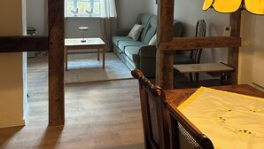 A room with a wooden ceiling, a dining table with chairs, a sofa, and a window with curtains. - Central and quiet: freshly renovated old apartment with charm (Helpsen)
