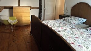 A bedroom with a wooden bed, a green chair, a wooden dresser, and a white door. - Central and quiet: freshly renovated old apartment with charm (Helpsen)