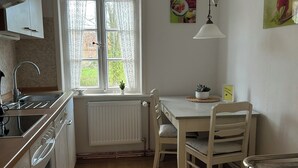 A kitchen with a window, a radiator, a sink, a stove, and a dining table with chairs. - Central and quiet: freshly renovated old apartment with charm (Helpsen)