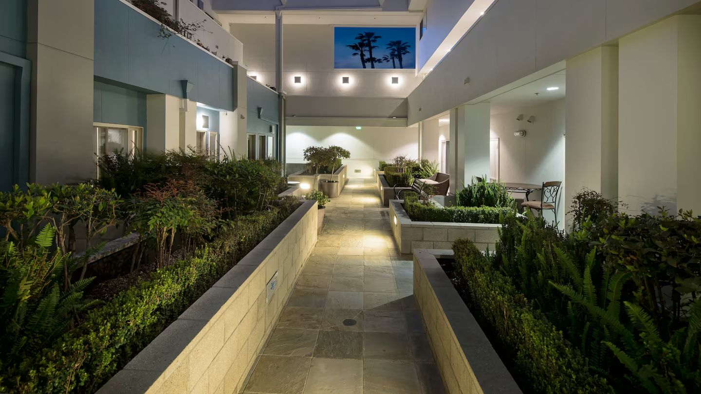 A corridor with a central pathway flanked by planters and seating areas, leading to a reception desk.