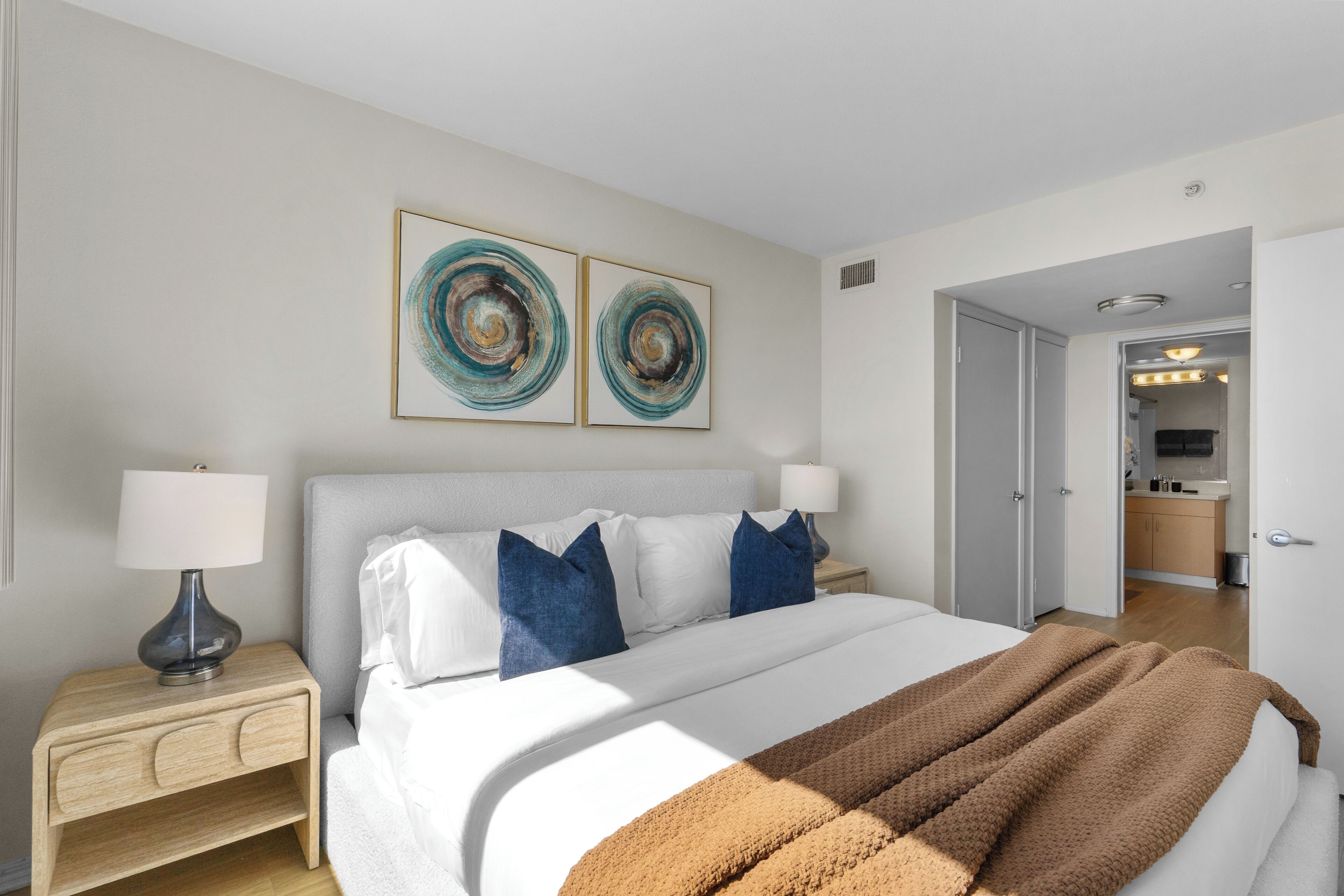 A modern hotel room with a large bed, two side tables, and a door leading to a bathroom.
