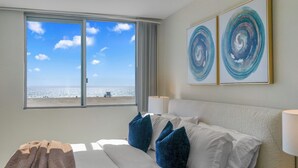 Quarto de hotel com cama, almofadas, vista para a praia e arte abstrata na parede.