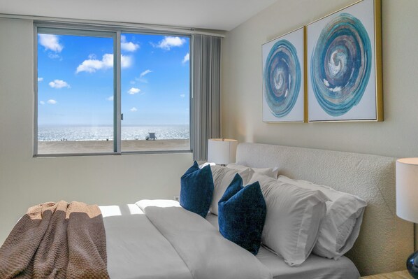 A hotel room with a bed, pillows, a view of the beach, and abstract art on the wall. - Sea Glass Jade' Oceanfront Full Beach/Ocean View Best location Right on the Sand (Santa Monica)