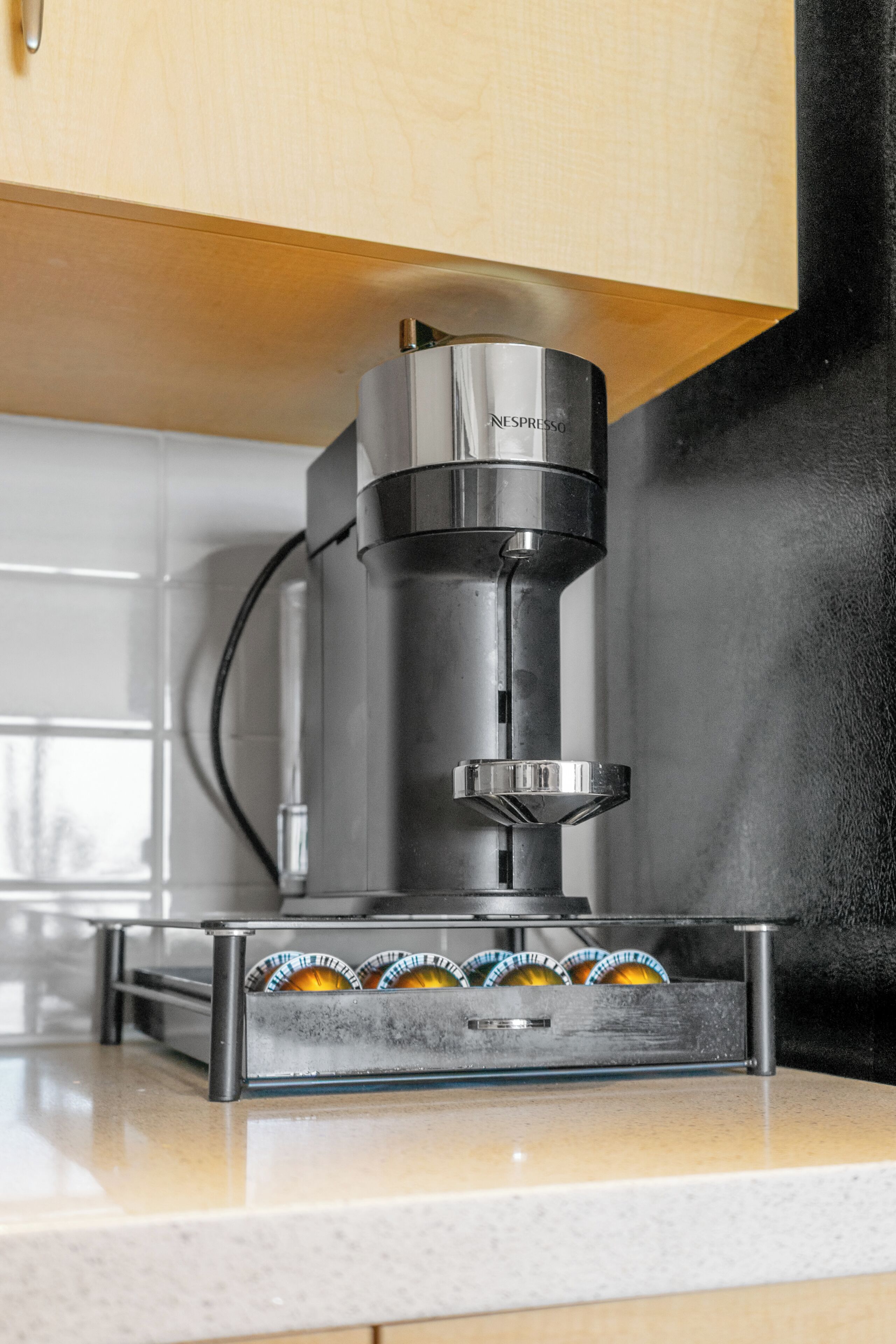 Une machine à café Nespresso posée sur un plan de travail de cuisine, avec une fenêtre en arrière-plan.