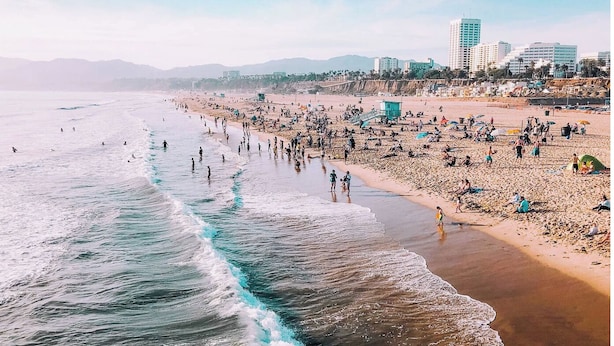 Uma praia com pessoas, uma torre salva-vidas e edifícios ao fundo.