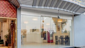 A modern building with a glass facade, a red decorative entrance, and a tiled patio area. - Deluxe With Twin Bed Kaveri Executive Lodging (Rajgurunagar)