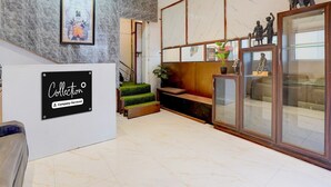 A reception area with a marble wall, a framed artwork, a staircase, and a glass display case with figurines. - Deluxe With Twin Bed Kaveri Executive Lodging (Rajgurunagar)