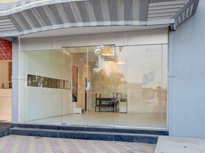 Un edificio moderno con entrada de vidrio, un interior visible con un banco y una mesa, y un piso con diseño.