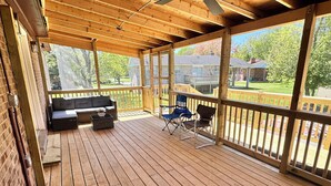 A covered deck with a wooden floor, a sofa, two chairs, and a small table. - 3-bedroom house in peaceful Fort Washington with AC comfort (Fort Washington)