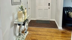A hallway with a white door, a mirror, a glass console table with decorative items, and a wooden floor. - 3-bedroom house in peaceful Fort Washington with AC comfort (Fort Washington)