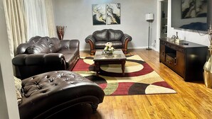 A living room with two leather sofas, a coffee table, a chandelier, artwork on the wall, and a TV. - 3-bedroom house in peaceful Fort Washington with AC comfort (Fort Washington)