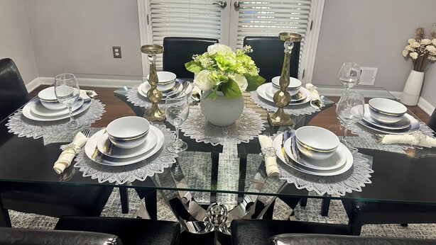 A dining table set with white plates, gold cutlery, and a vase with flowers. - 3-bedroom house in peaceful Fort Washington with AC comfort (Fort Washington)