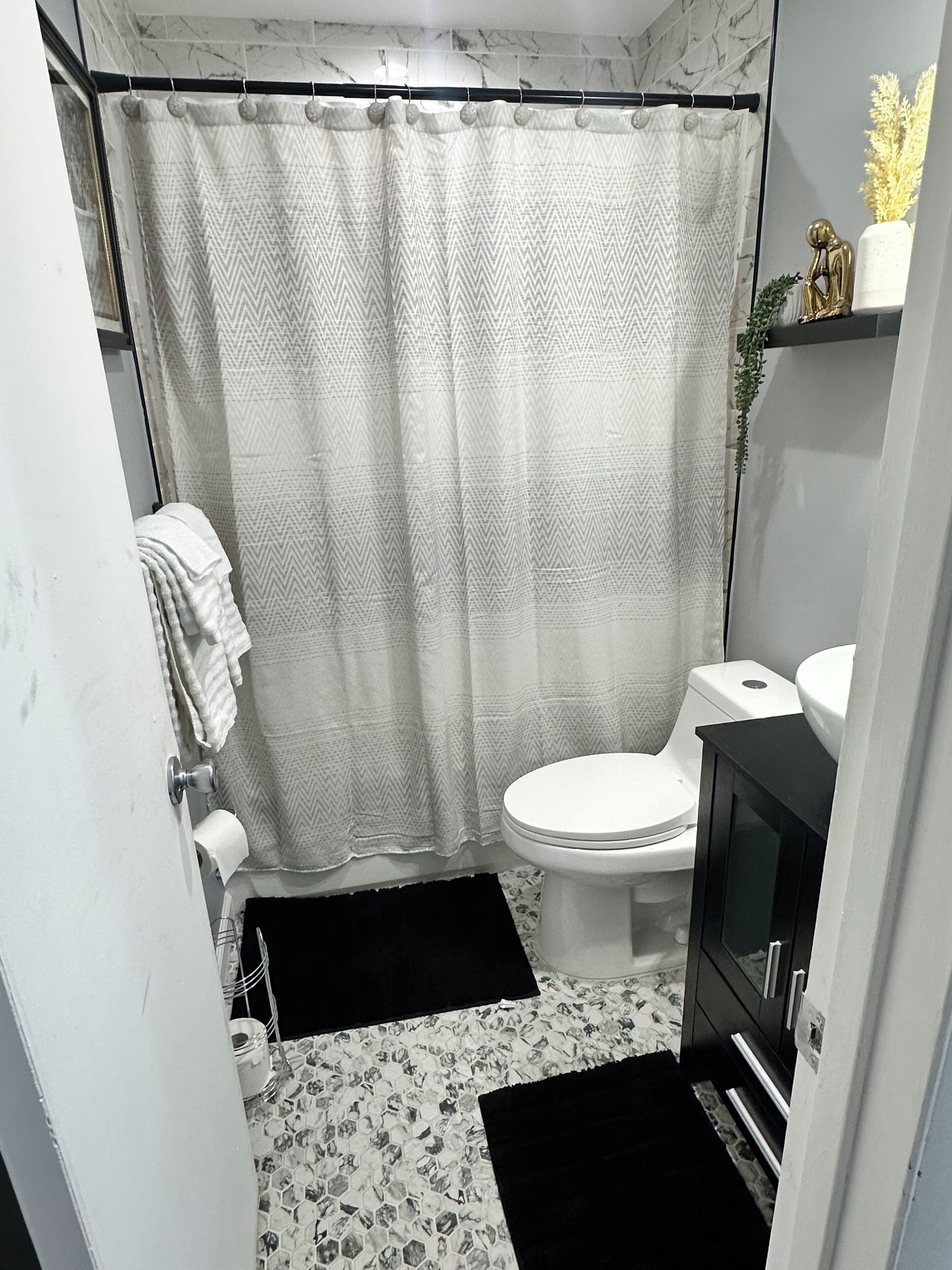 A compact bathroom with a shower curtain, toilet, sink, and a small television.