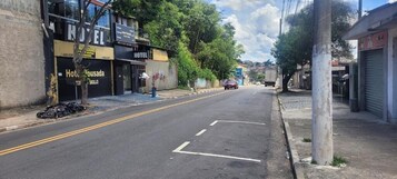Rua com um hotel chamado 'Hotel Bousada' à esquerda, uma estrada livre e um carro estacionado ao longe.