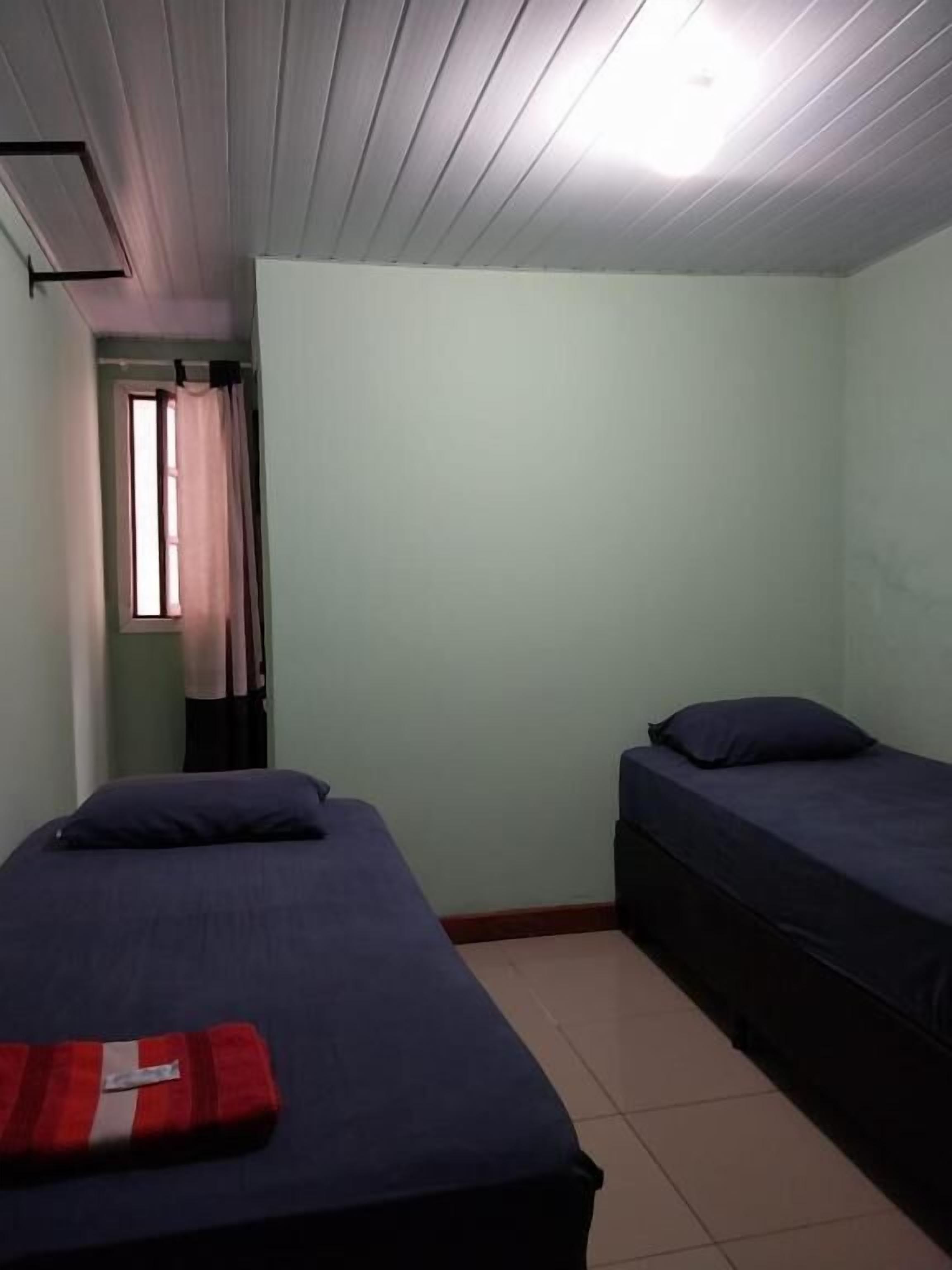 A room with two beds, a window with curtains, and a ceiling light.
