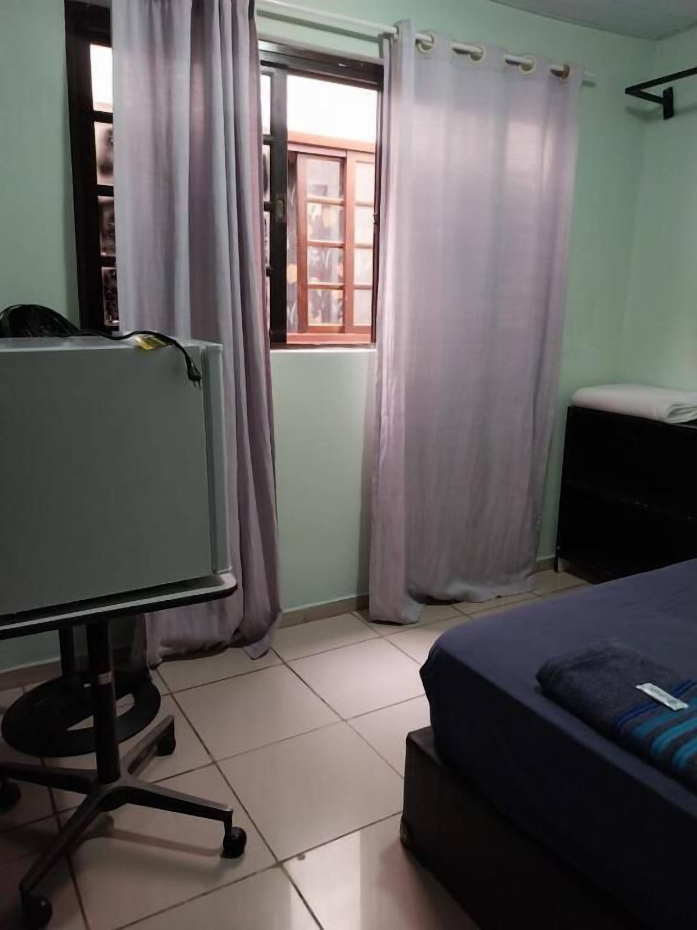 Una habitación con cama, escritorio, ventana con cortinas y radiador.