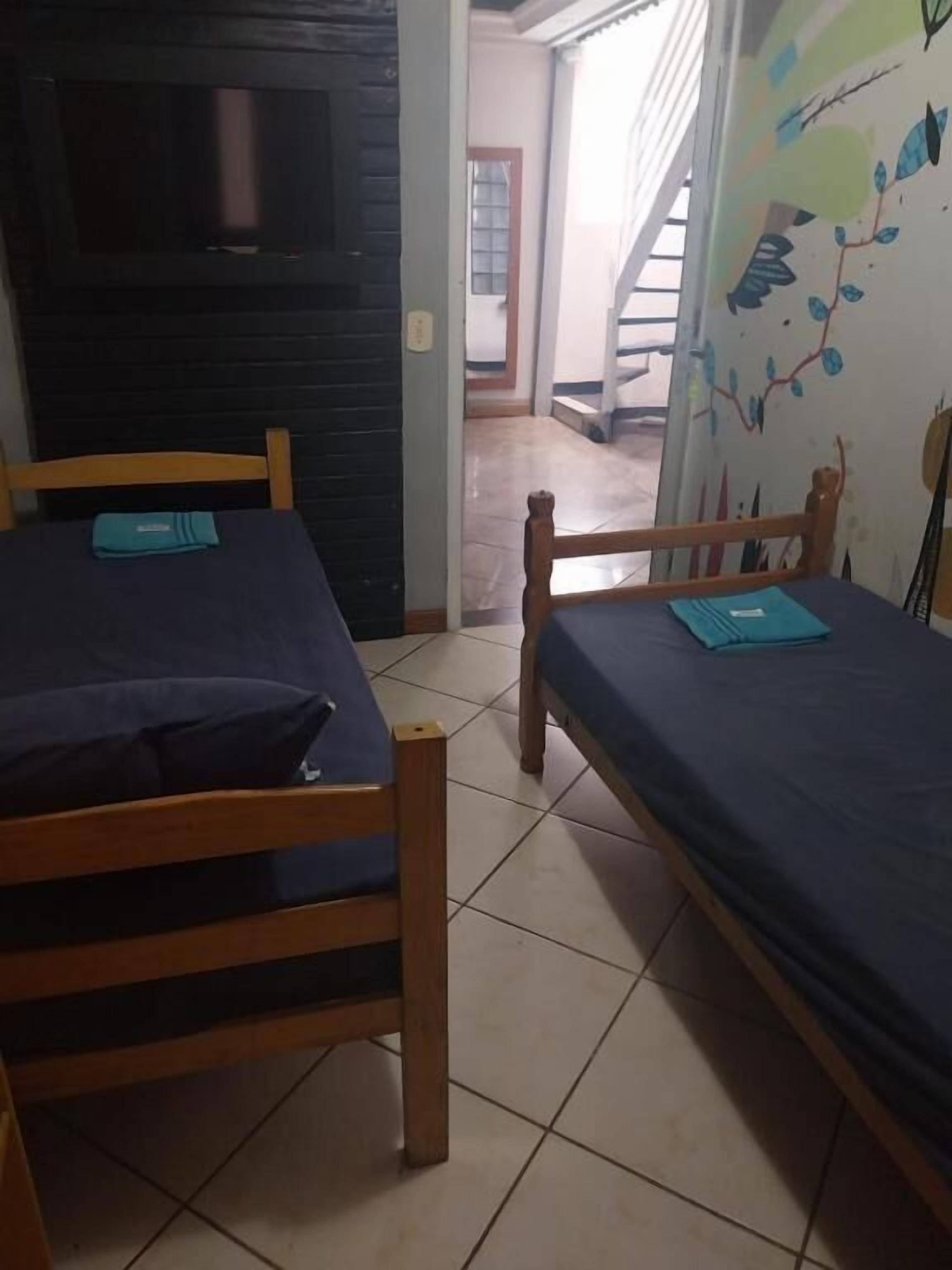 Two wooden beds with blue bedding, a tiled floor, and a wall with a painted tree and branches.