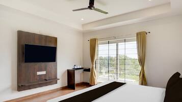 A hotel room with a bed, a TV mounted on the wall, a desk, and a window with curtains.