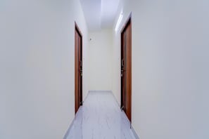 A hallway with white walls and a marble floor, leading to two wooden doors. - Deluxe Nira Residency (Coimbatore)