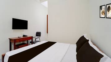 A hotel room with a bed, a desk, a chair, a flat-screen TV, and artwork on the wall.
