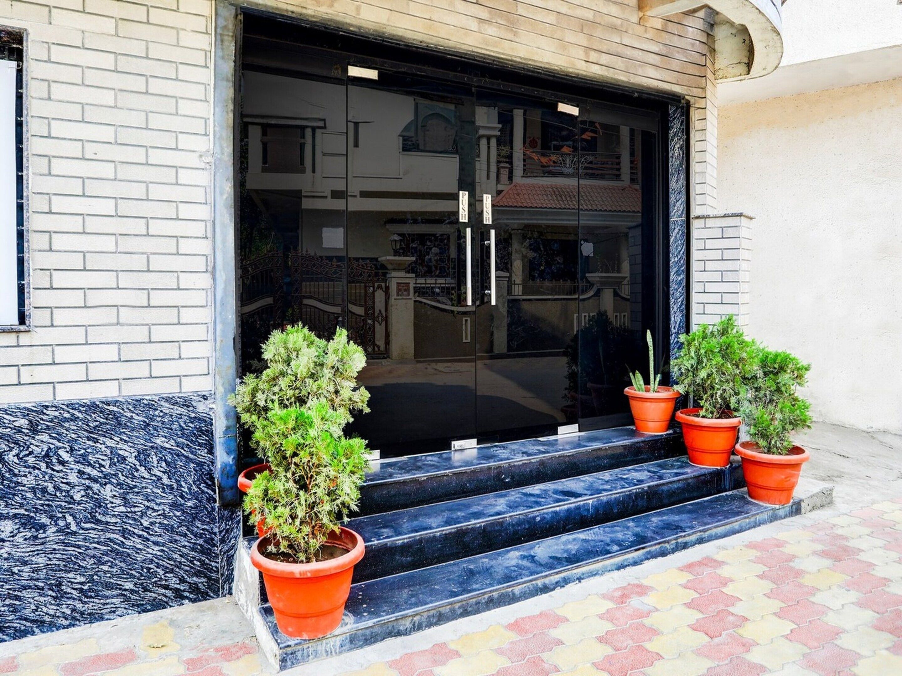 Entrada de un edificio con puerta de vidrio, escalones y plantas en macetas.
