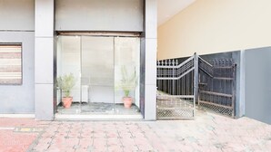 Entrada de edificio con techo de madera, puerta de vidrio, plantas en macetas y una reja de metal.