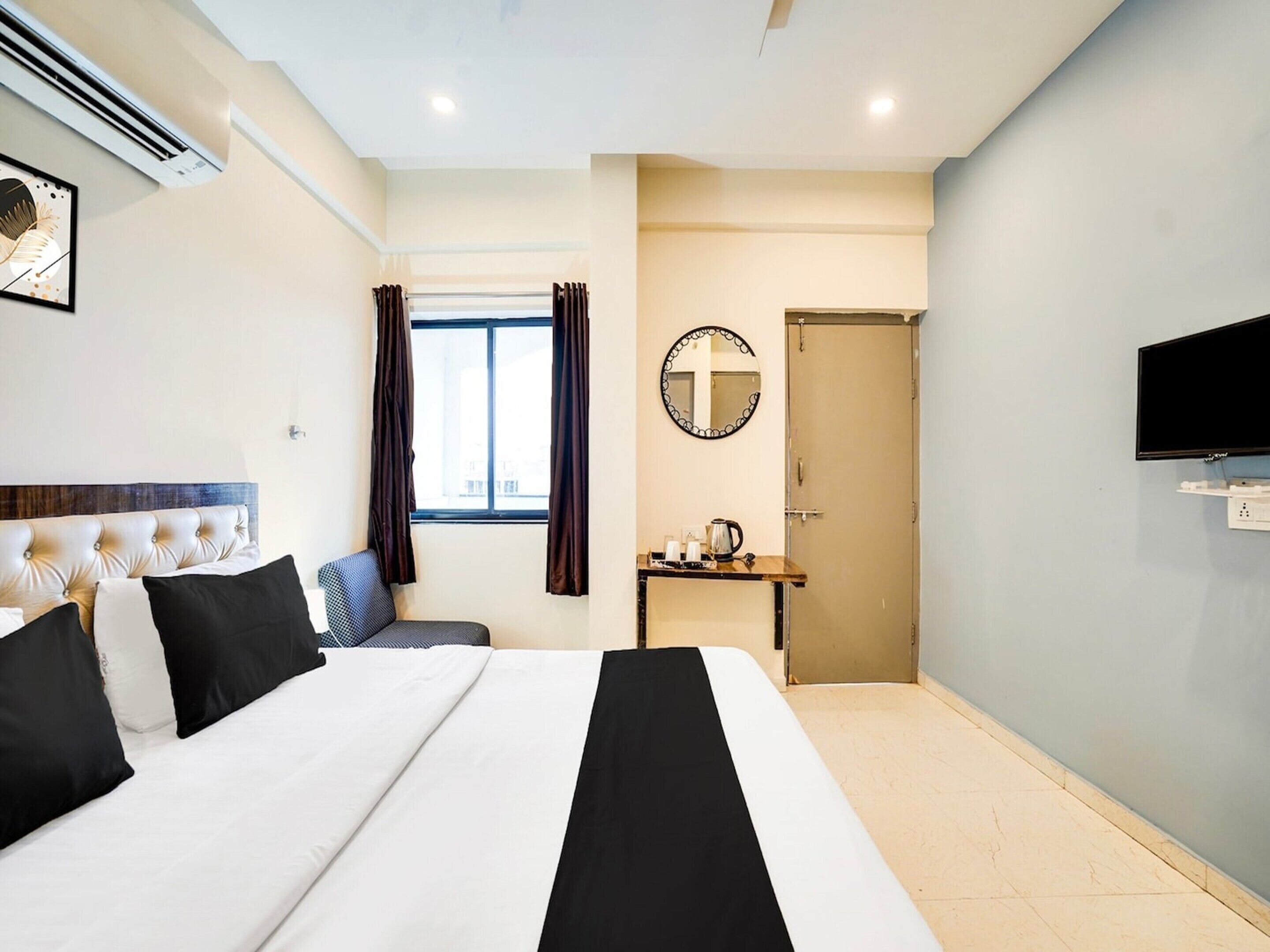 Habitación de hotel con cama, escritorio, espejo, televisor y ventana con cortinas.